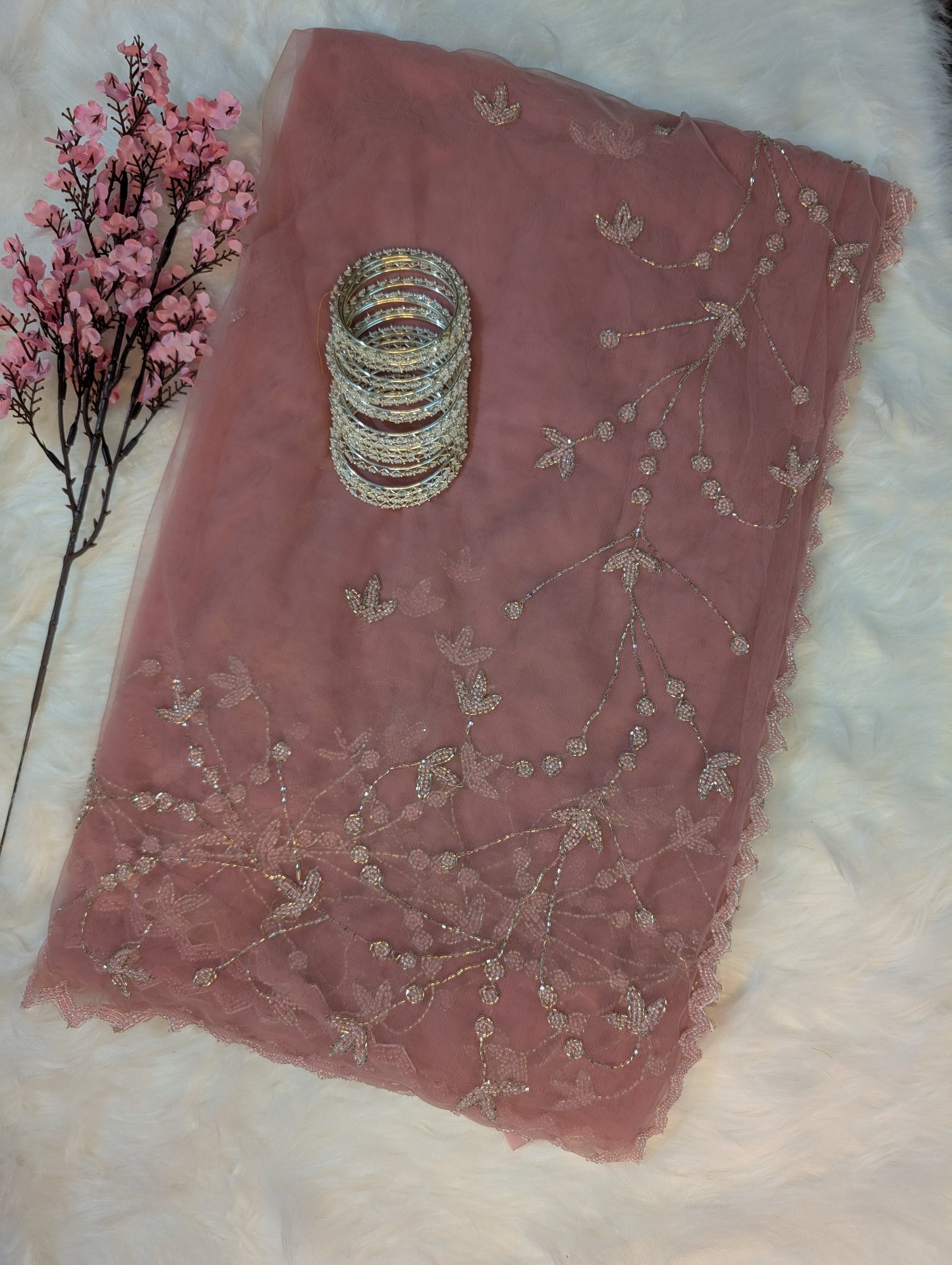 Pink embroidered fabric with a stack of silver bangles on a white surface.